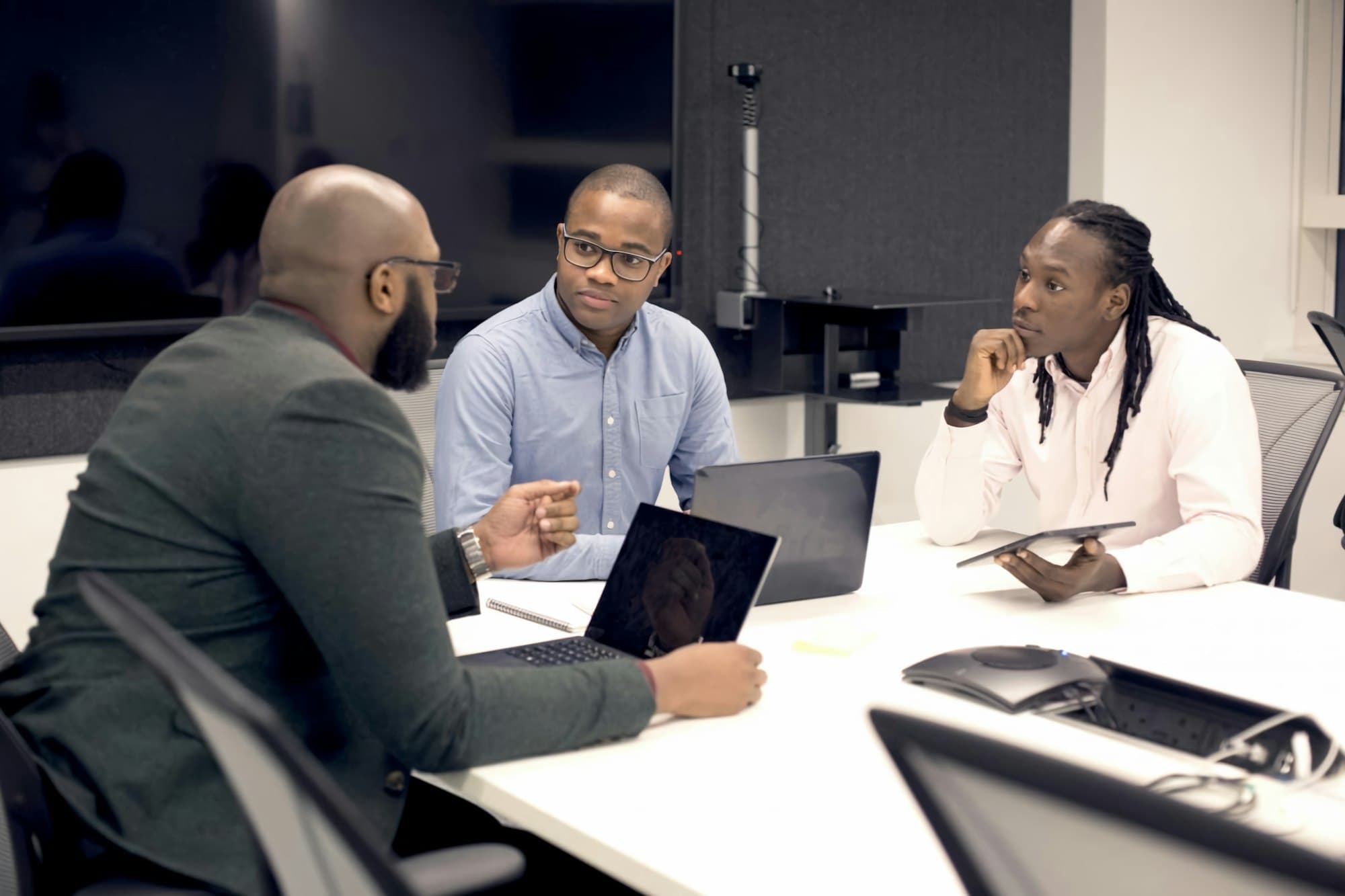 Three colleagues talking around a meeting table with laptops