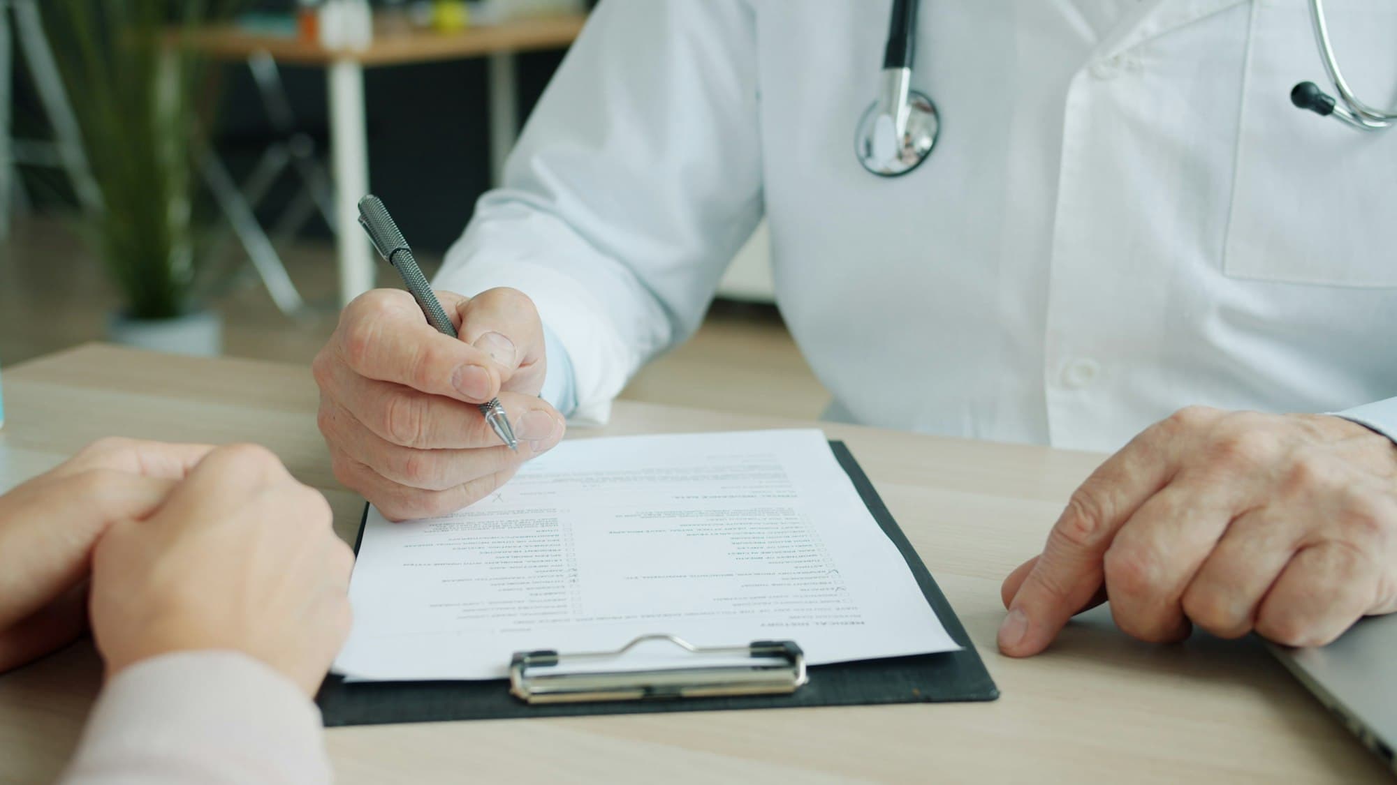 A doctor completing a form on a clipboard at a desk
