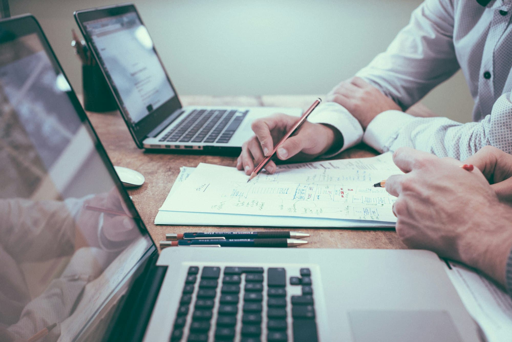 Two people reviewing documents with a pencil beside their laptops