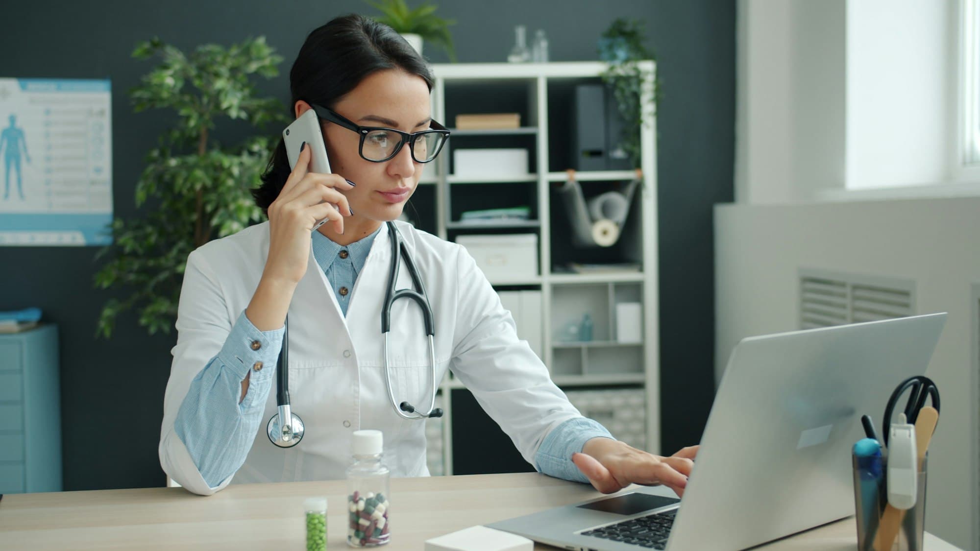 A doctor on the phone while checking the schedule on a laptop